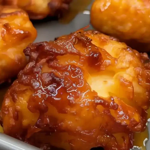 Close-up of golden-brown baked apple fritters drizzled with a sweet glaze, fresh out of the oven.