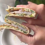 Hand holding a crispy egg tortilla wrap stuffed with turkey, spinach, and eggs on a rustic table.